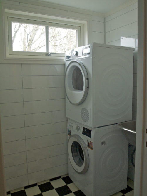 Austrått agrotourism, Kårstua, laundryroom with white walls, black and white floor, washing machine with a dryer on top