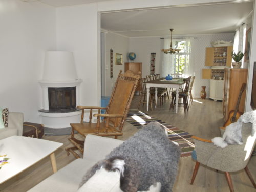 Holiday house, Austrått agrotourism, Kårstua, living room, white corner fireplace to the left, chairs with sheep skin, dining table in the background